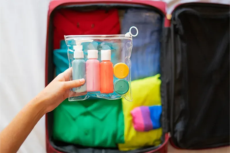 Person holding packed toiletry kit up to camera with a packed suitcase in the background